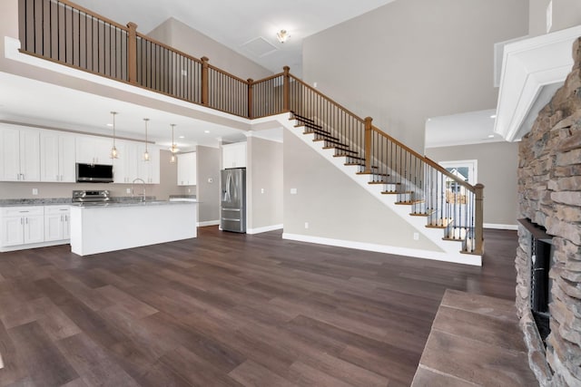 unfurnished living room featuring sink, a stone fireplace, dark wood-type flooring, and a high ceiling