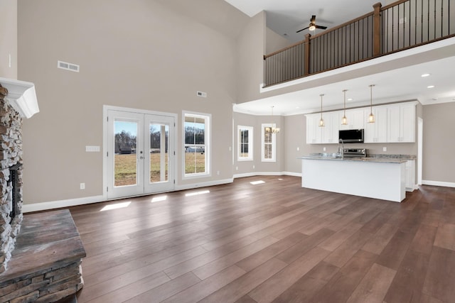 unfurnished living room featuring a stone fireplace, dark hardwood / wood-style floors, ceiling fan, and a high ceiling