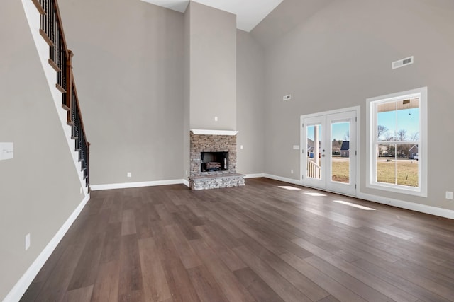 unfurnished living room with a towering ceiling, a fireplace, dark hardwood / wood-style floors, and french doors