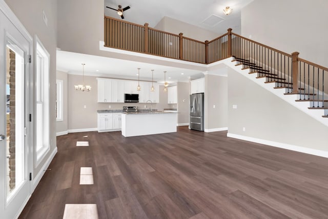 unfurnished living room with sink, a towering ceiling, dark wood-type flooring, and a chandelier