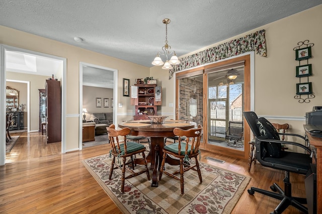 dining space with a chandelier, light hardwood / wood-style floors, and a textured ceiling