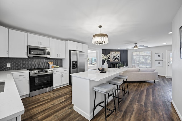 kitchen with decorative light fixtures, white cabinets, a kitchen bar, backsplash, and stainless steel appliances