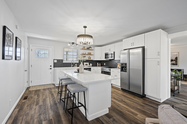 kitchen featuring a breakfast bar area, appliances with stainless steel finishes, white cabinetry, hanging light fixtures, and backsplash