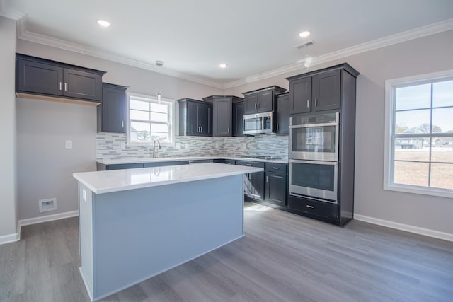 kitchen featuring stainless steel appliances, a kitchen island, light wood-type flooring, and decorative backsplash