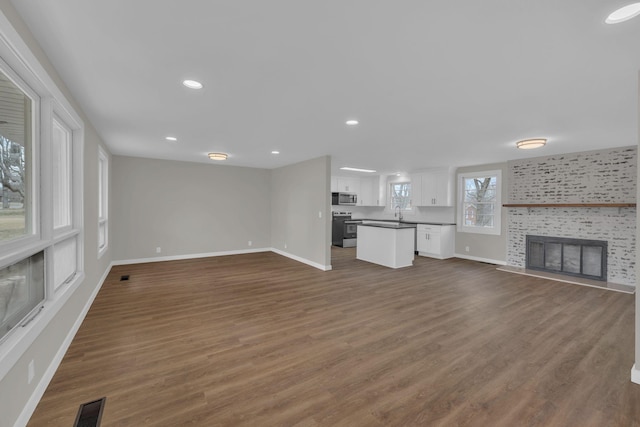 unfurnished living room featuring baseboards, visible vents, dark wood-type flooring, and a tile fireplace