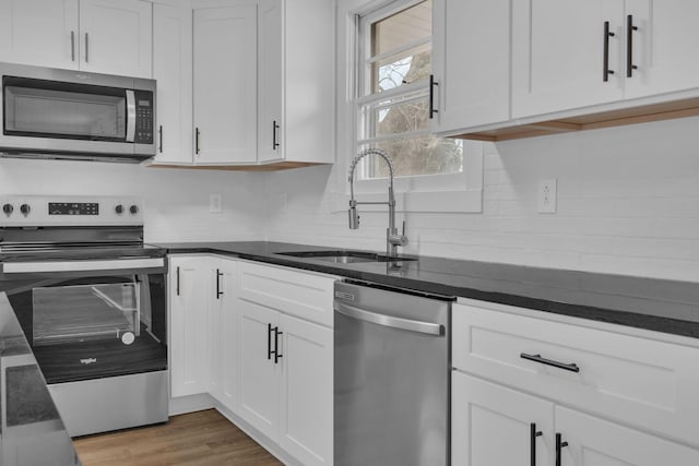 kitchen with wood finished floors, a sink, white cabinets, appliances with stainless steel finishes, and decorative backsplash