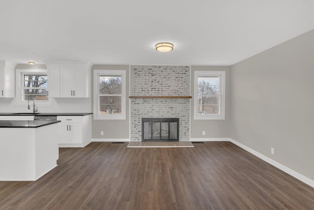 unfurnished living room featuring baseboards, a healthy amount of sunlight, a sink, and a tiled fireplace