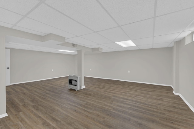 finished basement featuring baseboards, dark wood finished floors, a drop ceiling, and heating unit