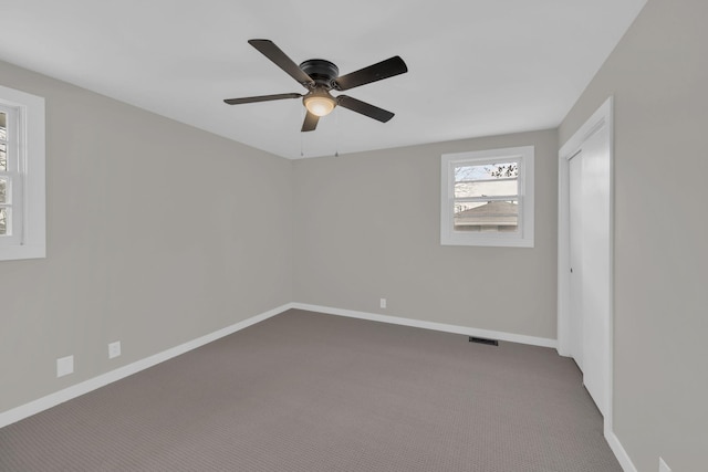 unfurnished room featuring visible vents, dark carpet, baseboards, and ceiling fan