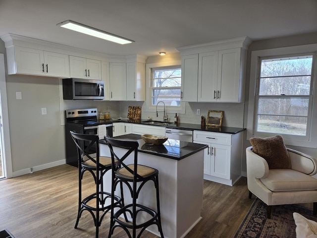 kitchen with stainless steel appliances, dark wood-style flooring, a sink, white cabinetry, and dark countertops