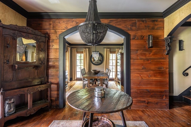 dining room with an inviting chandelier, dark wood-type flooring, ornamental molding, and wooden walls