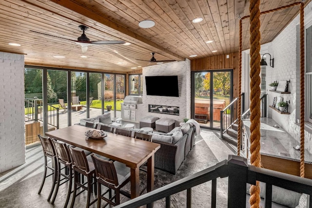 sunroom featuring wood ceiling, ceiling fan, a stone fireplace, and a wealth of natural light