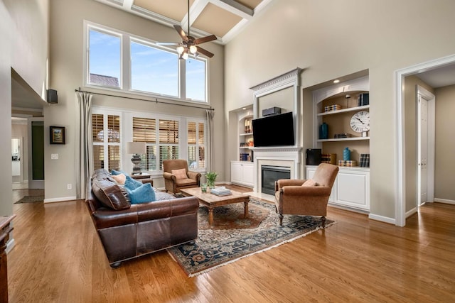 living room with ceiling fan, hardwood / wood-style floors, a towering ceiling, coffered ceiling, and built in shelves