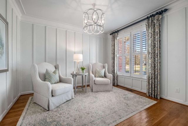 sitting room featuring an inviting chandelier, a decorative wall, wood finished floors, and ornamental molding