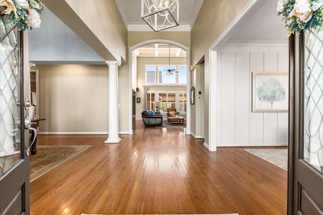 foyer entrance featuring crown molding, wood-type flooring, ceiling fan, a towering ceiling, and decorative columns