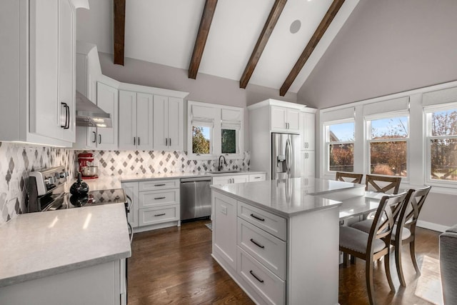 kitchen featuring a breakfast bar, range hood, appliances with stainless steel finishes, plenty of natural light, and a sink