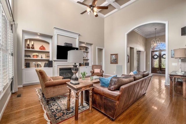 living room featuring coffered ceiling, a towering ceiling, crown molding, and light hardwood / wood-style floors