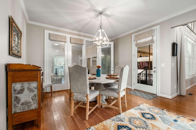 dining area with a notable chandelier, baseboards, wood-type flooring, and ornamental molding