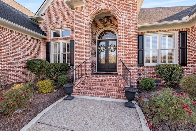 entrance to property with brick siding, french doors, and roof with shingles