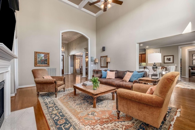 living room with coffered ceiling, crown molding, wood-type flooring, a towering ceiling, and a fireplace