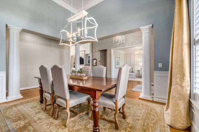 dining area with a decorative wall, wood finished floors, an inviting chandelier, and decorative columns