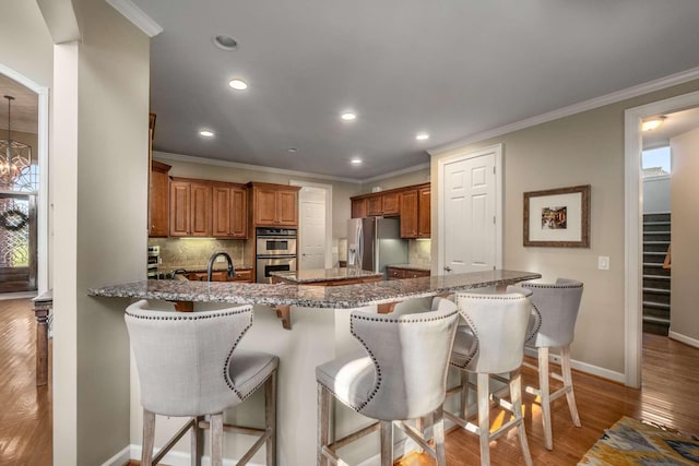 kitchen featuring a breakfast bar area, backsplash, light hardwood / wood-style floors, stainless steel appliances, and crown molding