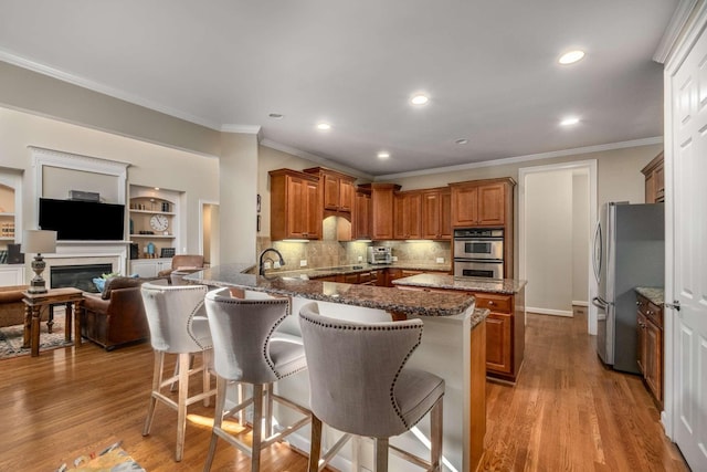 kitchen featuring a breakfast bar, light hardwood / wood-style flooring, dark stone countertops, kitchen peninsula, and stainless steel appliances