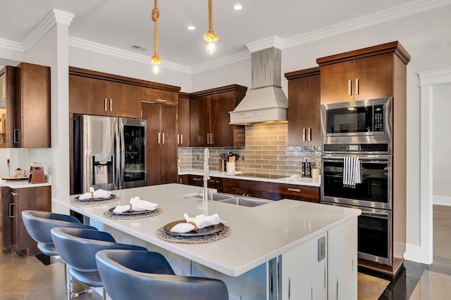 kitchen with an island with sink, appliances with stainless steel finishes, premium range hood, and pendant lighting