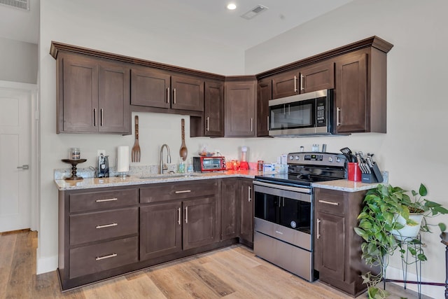 kitchen with sink, light stone counters, dark brown cabinetry, stainless steel appliances, and light wood-type flooring