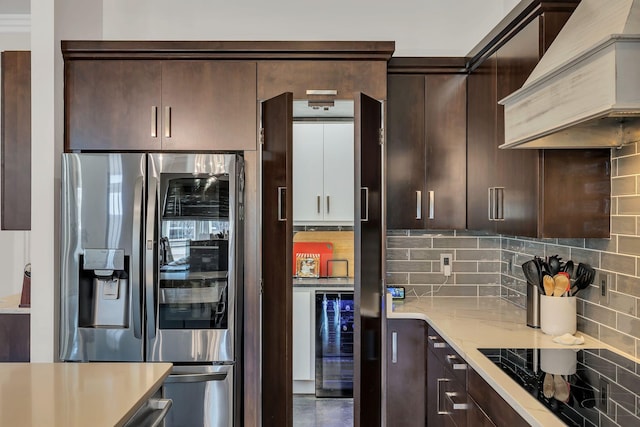 kitchen with tasteful backsplash, beverage cooler, black appliances, dark brown cabinets, and custom range hood