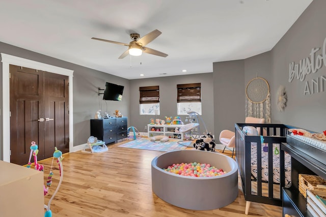 bedroom with light hardwood / wood-style floors, a nursery area, and ceiling fan