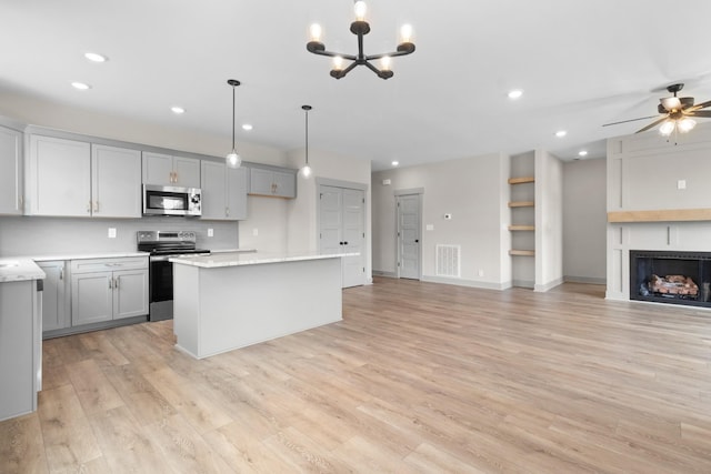 kitchen with gray cabinetry, stainless steel appliances, a kitchen island, decorative light fixtures, and light wood-type flooring