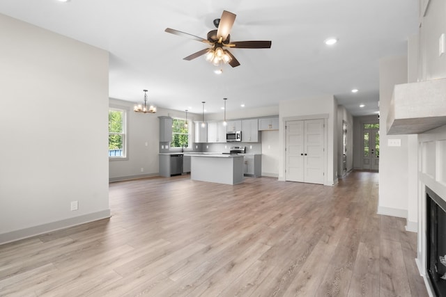 unfurnished living room with ceiling fan with notable chandelier and light hardwood / wood-style floors