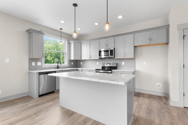 kitchen with light stone counters, decorative light fixtures, a center island, stainless steel appliances, and backsplash