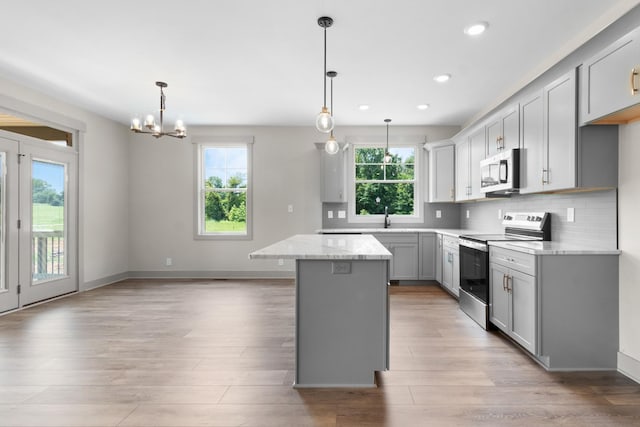 kitchen featuring stainless steel appliances, light stone countertops, a kitchen island, and hanging light fixtures