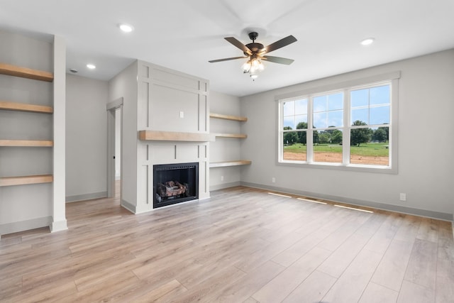 unfurnished living room featuring ceiling fan, a large fireplace, light hardwood / wood-style floors, and built in features