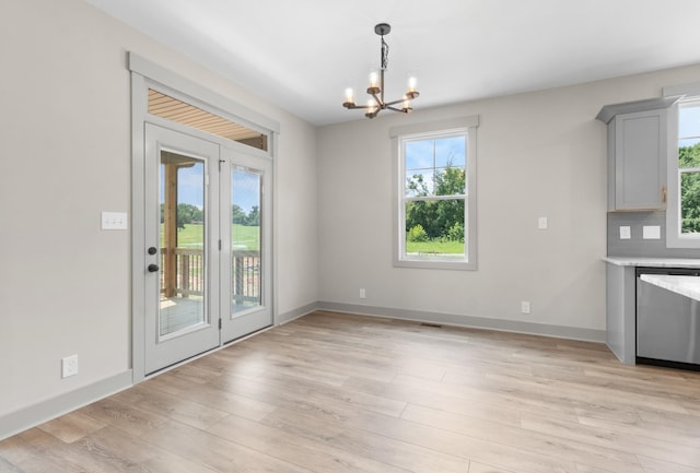 unfurnished dining area featuring an inviting chandelier, a healthy amount of sunlight, and light hardwood / wood-style flooring