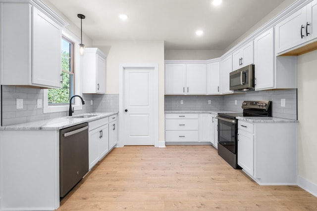 kitchen featuring sink, appliances with stainless steel finishes, white cabinetry, light stone countertops, and light hardwood / wood-style floors