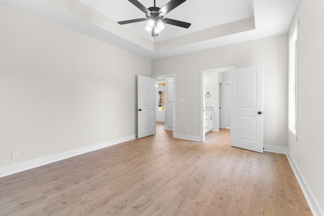 unfurnished bedroom featuring ceiling fan, a raised ceiling, light hardwood / wood-style floors, and multiple windows