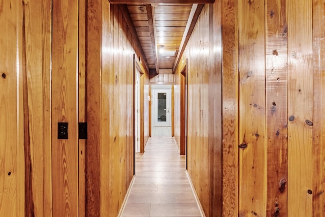 hallway with light wood-type flooring, wooden ceiling, and wood walls