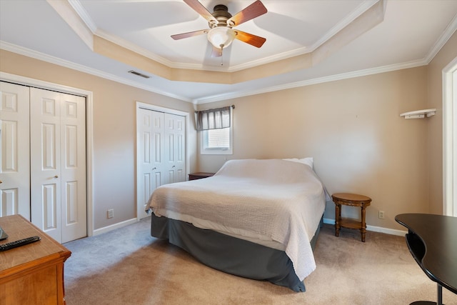 carpeted bedroom with a raised ceiling, ornamental molding, multiple closets, and ceiling fan