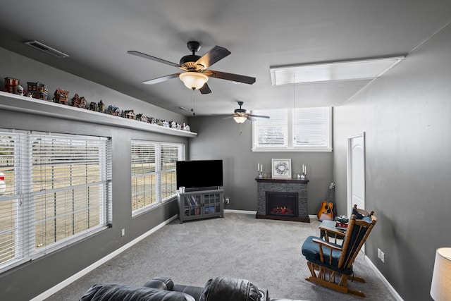 living room with light carpet, a stone fireplace, plenty of natural light, and ceiling fan