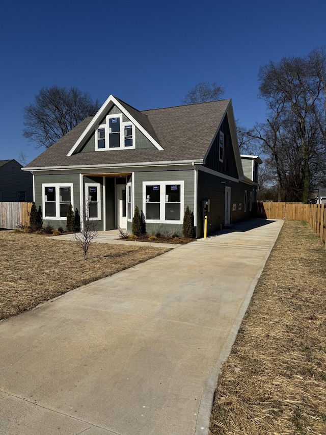 view of front of property featuring a shingled roof, fence, and concrete driveway