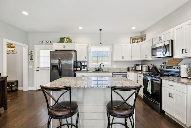 kitchen featuring appliances with stainless steel finishes, a breakfast bar, decorative light fixtures, white cabinets, and a center island