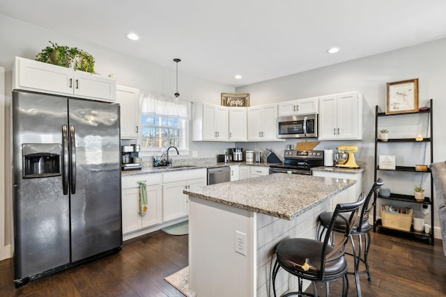 kitchen with a kitchen island, white cabinetry, stainless steel appliances, light stone countertops, and dark wood-type flooring