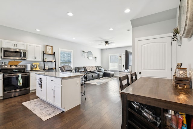 kitchen featuring appliances with stainless steel finishes, white cabinetry, a breakfast bar area, a center island, and light stone countertops