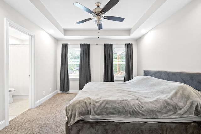 carpeted bedroom with a raised ceiling, ceiling fan, and ensuite bath