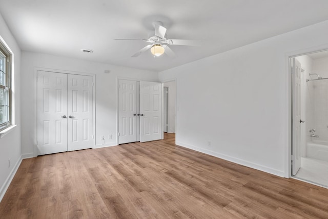 unfurnished bedroom with ensuite bath, light hardwood / wood-style flooring, ceiling fan, and two closets