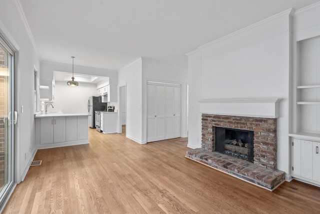 unfurnished living room featuring crown molding, a brick fireplace, sink, and light hardwood / wood-style flooring