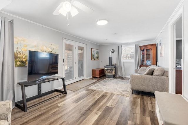 living room with hardwood / wood-style flooring, ceiling fan, crown molding, and a wood stove